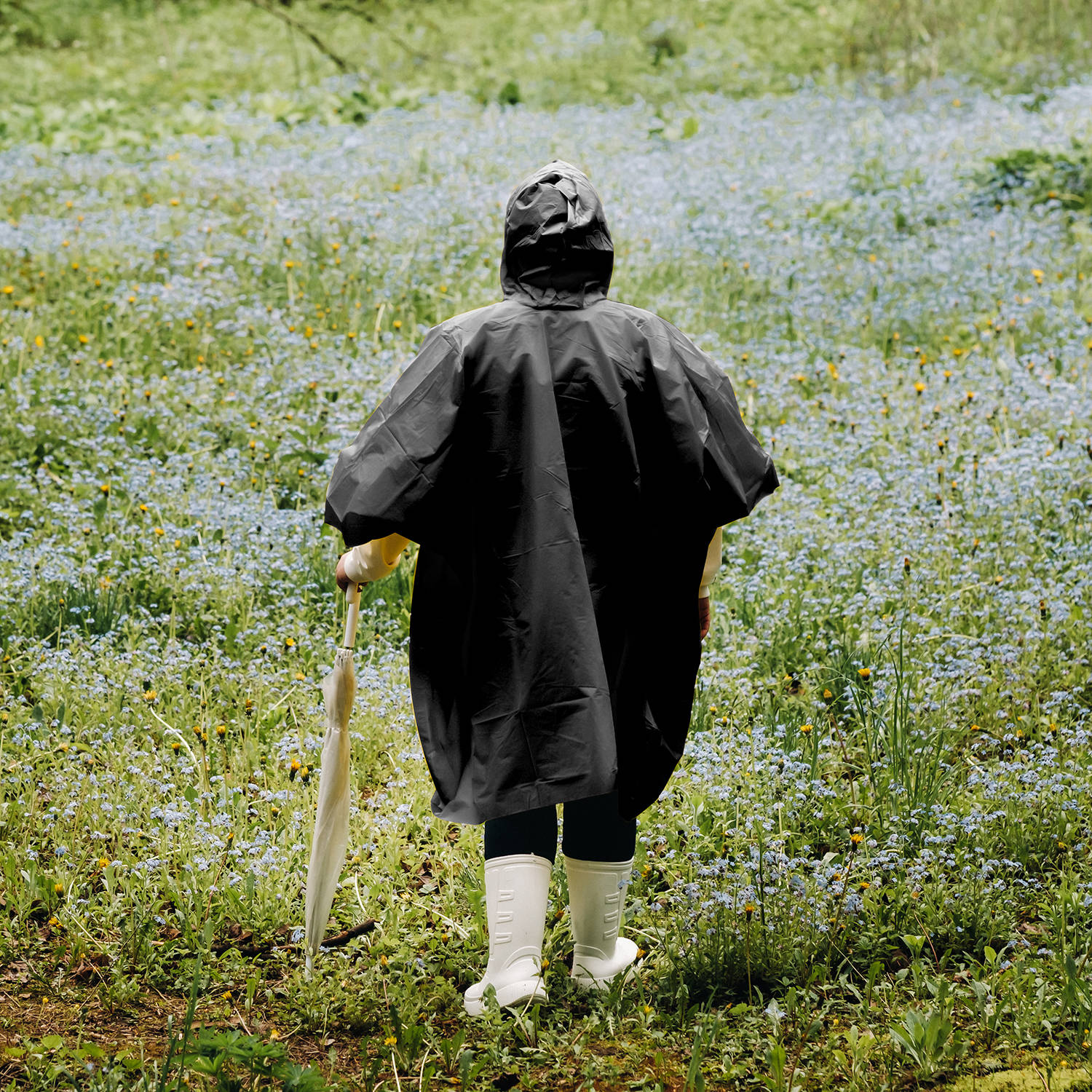 a woman in a yellow raincoat walks in the park and garden in the summer