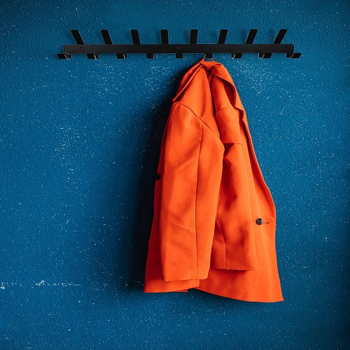Metal hooks on the background of a blue wall. A red women’s jacket is hanging on a hanger.
