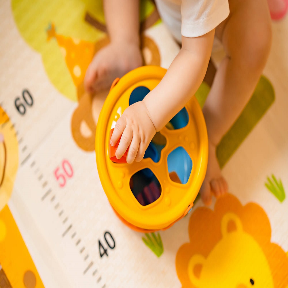 Cute little baby boy playing with colorful educational toys on the play mat in the home interior. Educational toys for little children. Early childhood development. Home activity for children